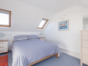 A bedroom with a bed, bedside tables, a nightstand, a dresser, a window, a skylight, and a framed picture on the wall.