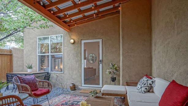 An outdoor patio area with wicker furniture, a white sofa, and a patterned rug. - Boho 2b/2ba Downtown/OldTown, Patio w/fire feature (Albuquerque)