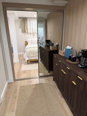 A hotel room with a mirrored wardrobe, a bed with a white duvet, a coffee machine, and a small table with a basket and magazines. - Fresh Walkable Fremont Home Near Ballard/Downtown (Seattle)