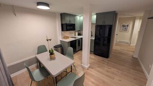 A modern kitchen with grey cabinets, a black refrigerator, and a dining area with a white table and green chairs. - Fresh Walkable Fremont Home Near Ballard/Downtown (Seattle)