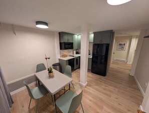 A modern kitchen with grey cabinets, a black refrigerator, and a dining area with a white table and green chairs. - Fresh Walkable Fremont Home Near Ballard/Downtown (Seattle)