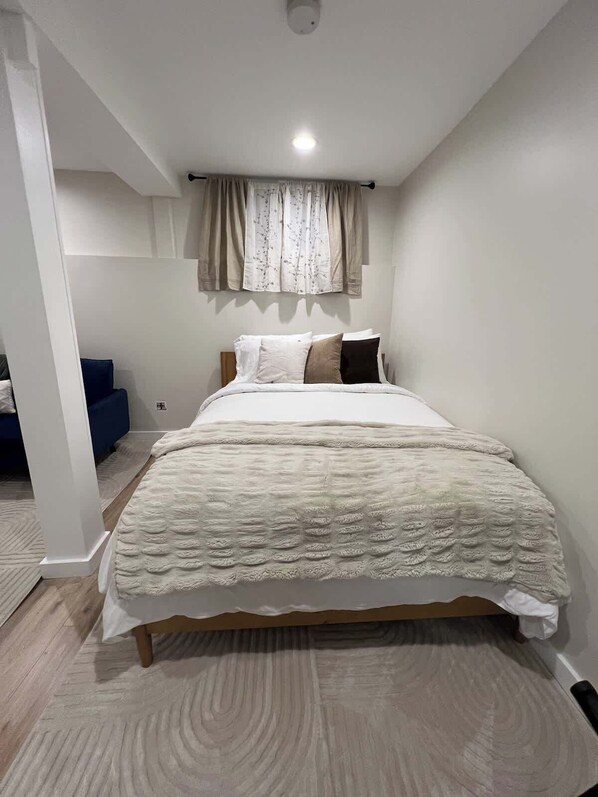 Un dormitorio con cama, ventana con cortinas, lámpara de techo y suelo de madera.
