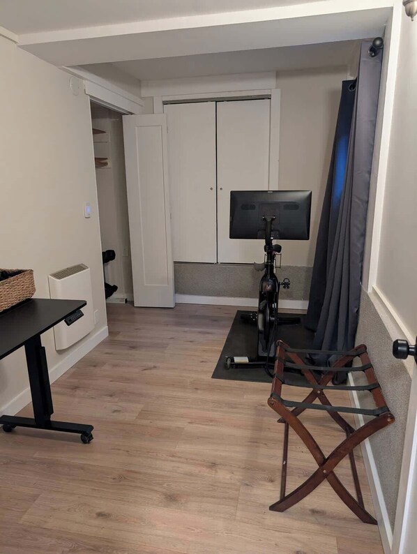 Ein Zimmer mit Schreibtisch, Stuhl, Fernseher auf einem Schrank und Vorhang.
