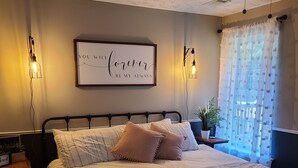 Et pænt opredt soveværelse med seng, sengeborde, en læselampe, et indrammet inspirerende citat og et vindue med let gardin.