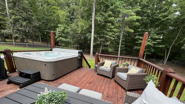 En terrasse med jacuzzi, fletmøbler og en potteplante.