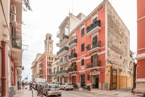 A street with parked cars and motorcycles, buildings with balconies, and a tower in the background. - MADAME BARI' Apt a step from the sea (Bari)