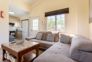 A living room with a beige sofa, a marble coffee table, and a kitchen in the background. - Villa Amorosa - Four Bedroom Villa, Sleeps 8 (Neo Chorio)
