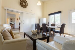 A modern living room with a dining area, featuring a sofa set, a coffee table, and a dining table with chairs. - Villa Amorosa - Four Bedroom Villa, Sleeps 8 (Neo Chorio)