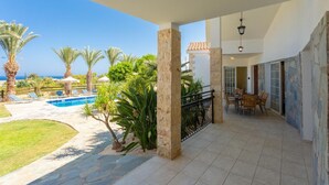 Un espace extérieur abrité comprenant une piscine, des palmiers et une terrasse avec des chaises et une table.