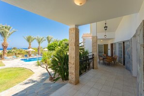 A covered outdoor area with a pool, palm trees, and a patio with chairs and a table.