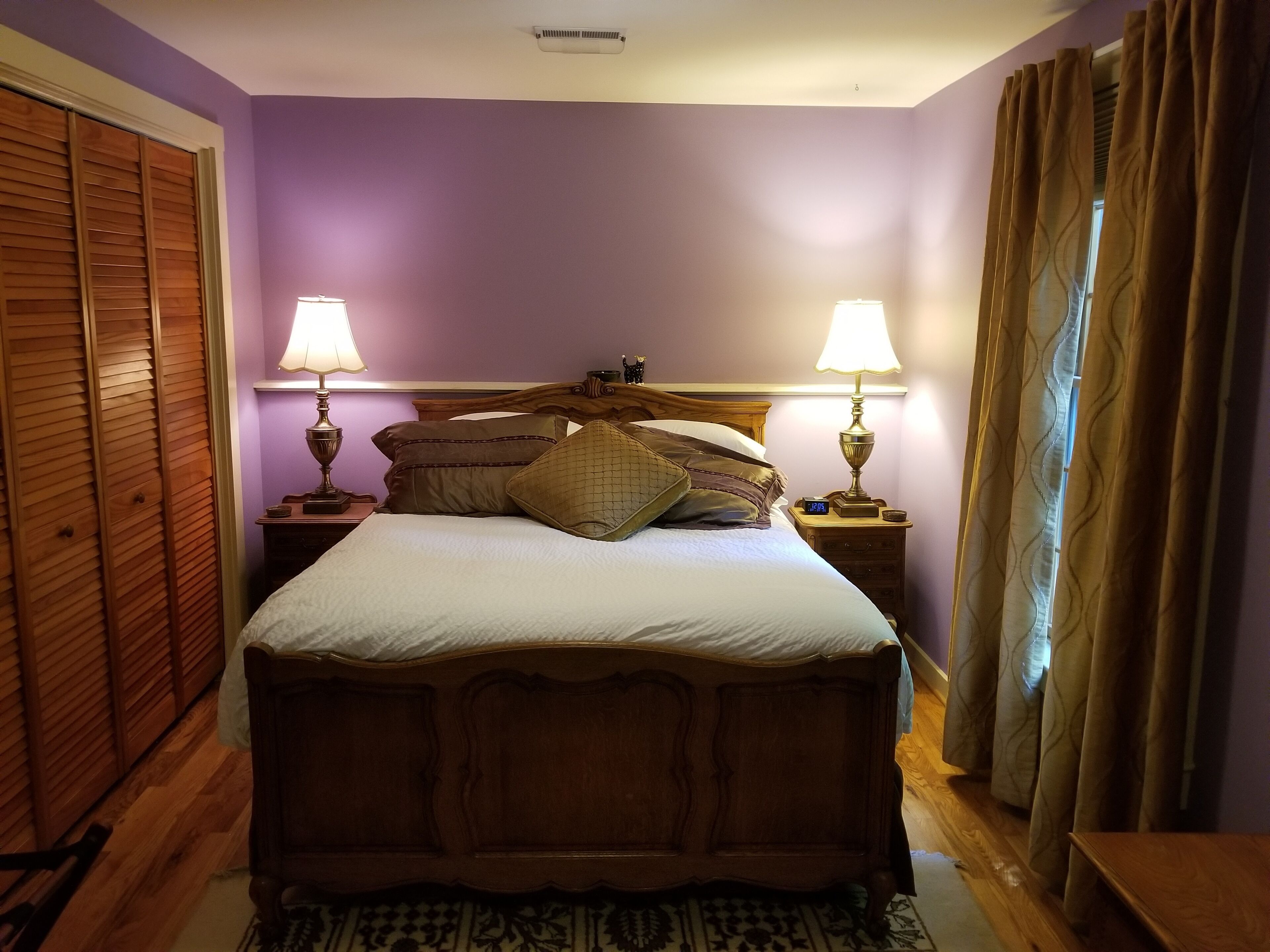 A bedroom with a wooden bed, purple walls, two bedside lamps, and a nightstand with a clock.