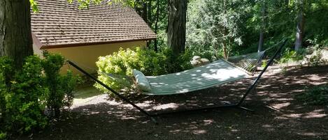 A hammock in a wooded area with a building in the background.