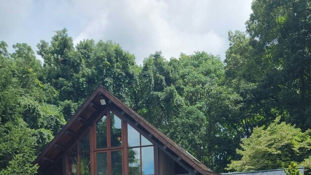 Una cabaña de madera de dos pisos con base de piedra, un balcón con mobiliario exterior y una piscina.