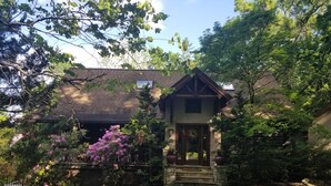 Una casa con porche de piedra, rodeada de árboles y plantas en flor.