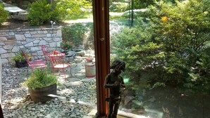 Una estatua de un hombre sosteniendo un pipa en un jardín con un muro de piedra, sillas rojas y plantas en macetas.
