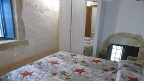 Ein Schlafzimmer mit einem Bett, das mit einer Bettdecke mit Sternfischmuster bezogen ist, einer weißen Tür und einem Kamin aus Stein.