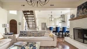 A spacious living room with a sofa, coffee table, and blue chairs. A staircase leads to an upper level.