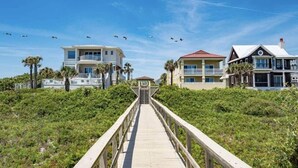 A wooden boardwalk leading to beachfront properties with balconies and a clear sky.