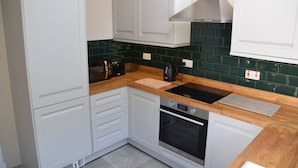 Una cocina moderna con armarios blancos, encimera de madera, horno empotrado y salpicadero con azulejos verdes.