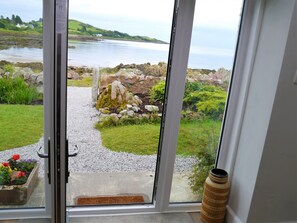 A view through a glass door of a coastal landscape with a gravel path, a stone wall, and a large vase. - Albany Cottage -  a cottage that sleeps 7 guests  in 4 bedrooms (Dalbeattie)