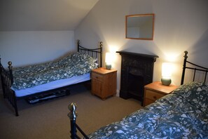Quarto com duas camas de solteiro, uma mesinha de cabeceira de madeira com abajur, cômoda e espelho na parede.