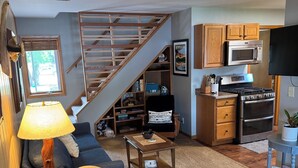 A living room with a sofa, a coffee table, and a staircase leading to a kitchen area. - Cabin on the Mississippi River (Trempealeau)