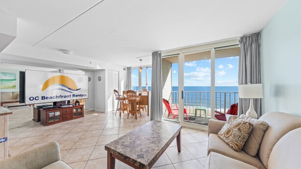 Un soggiorno spazioso con una grande TV, un'area pranzo e un balcone vista oceano.