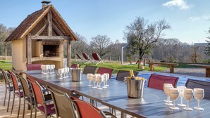 An outdoor dining area with a long table, chairs, and a grill structure.
