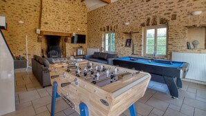 A cozy room with a foosball table, a pool table, a fireplace, and stone walls.