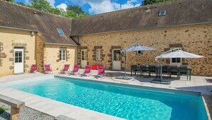 A swimming pool with lounge chairs and umbrellas, surrounded by stone walls and a tiled deck.