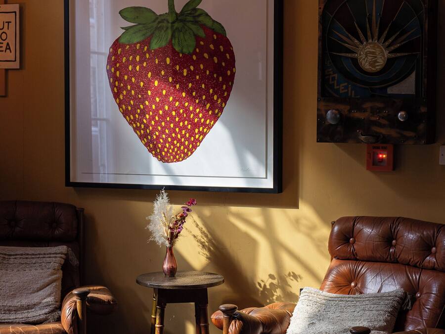 A cozy living room with a large framed strawberry artwork, a vintage radio, and a small round table with a vase.