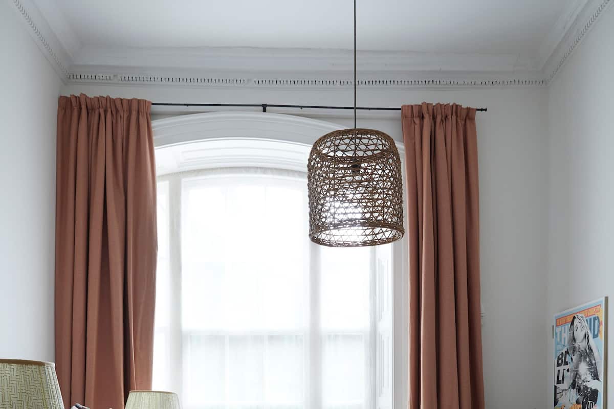 Ett välordnat sovrum med en säng, två sänglampor, en hängande taklampa, ett skrivbord med en stol och ett fönster med gardiner.