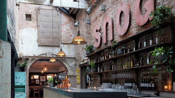 A bar with exposed brick walls, wooden beams, and a large 'snog' sign. There are shelves with bottles and glasses, and a wooden counter. - Artist Residence Bristol (Bristol)