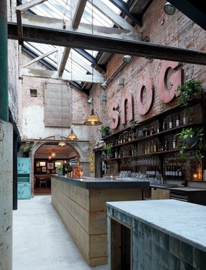 A bar with exposed brick walls, wooden beams, and a large 'snog' sign. There are shelves with bottles and glasses, and a wooden counter. - Artist Residence Bristol (Bristol)