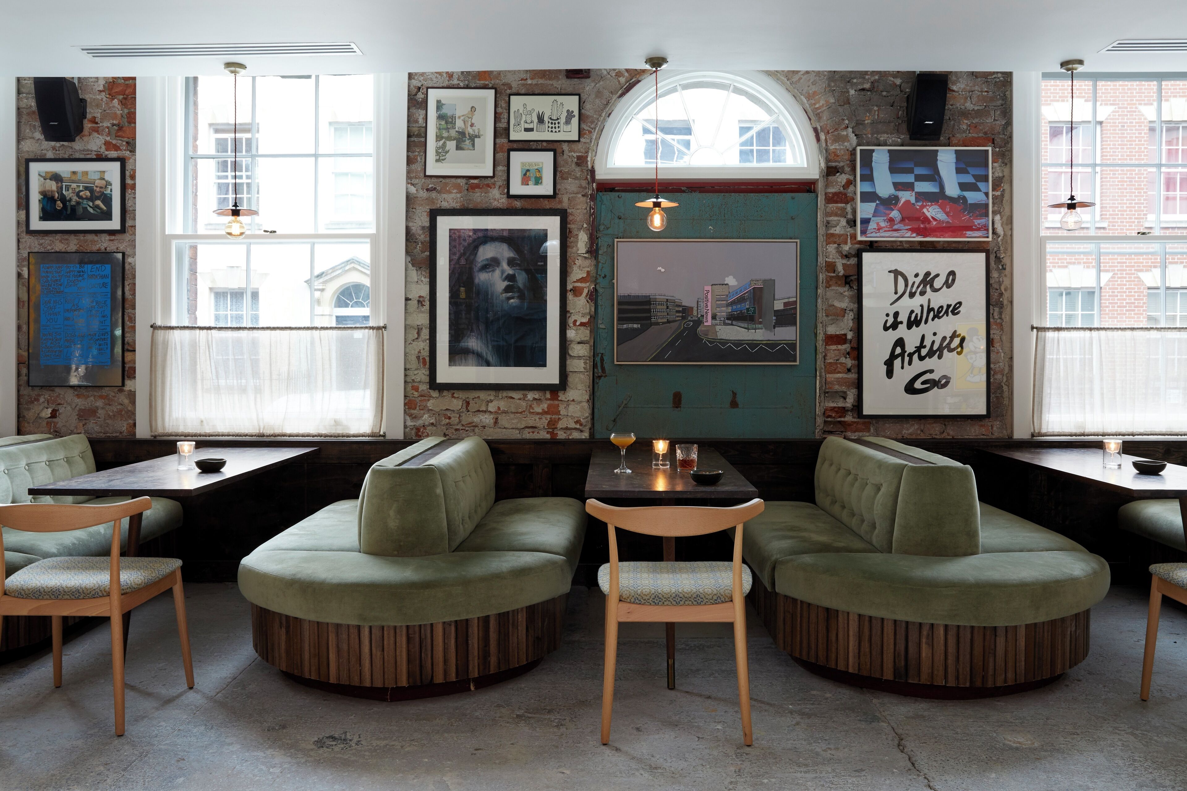 A cozy interior with green upholstered seating, a wooden table, and framed artwork on the walls.