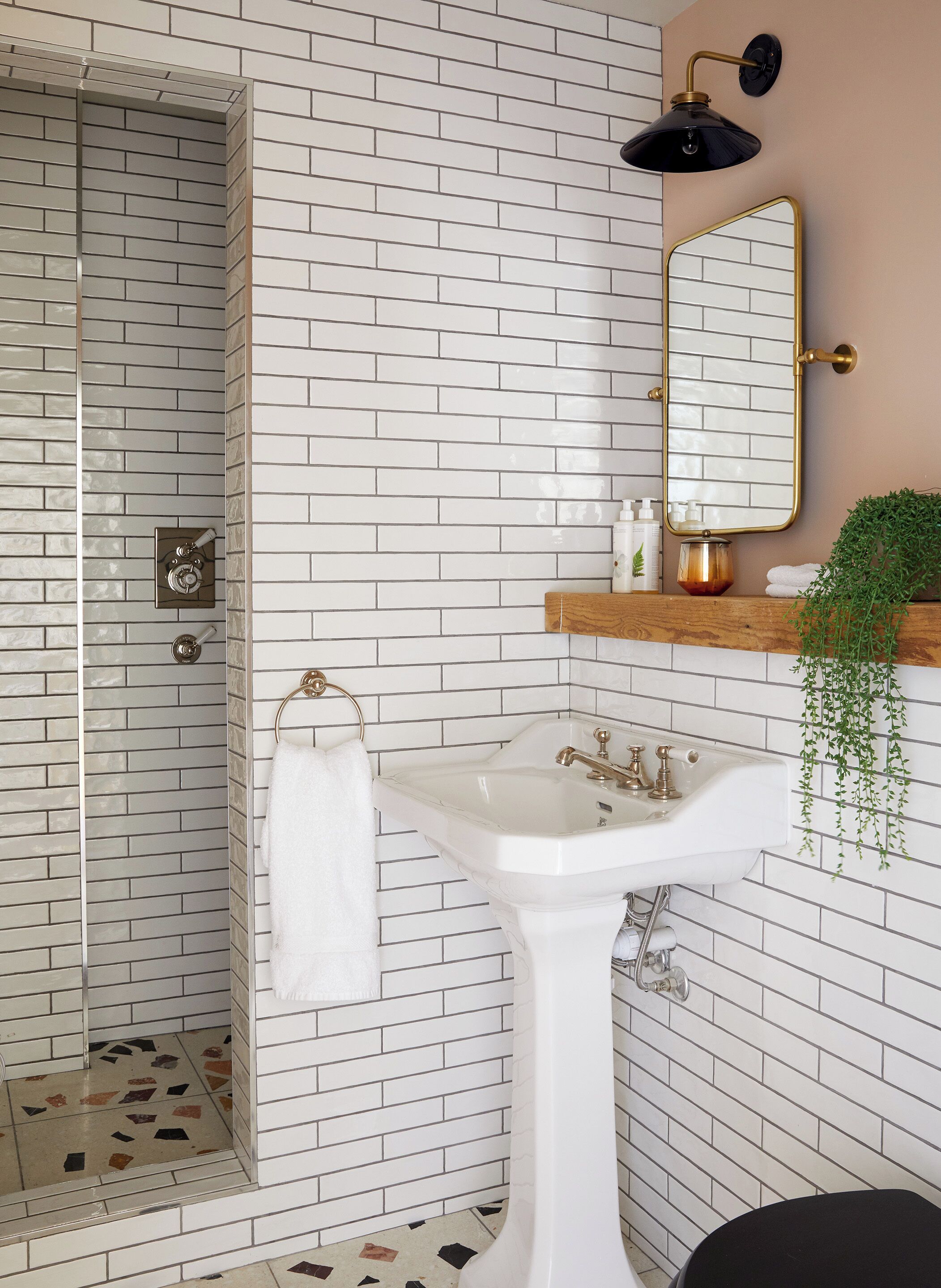 Un baño con paredes de ladrillo blanco, un lavabo blanco, un espejo, una ducha y una planta colgante.
