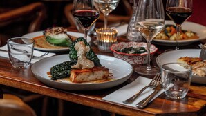 A restaurant table set with plates of food, wine glasses, and a vase with flowers. - Artist Residence Bristol (Bristol)
