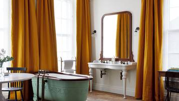 A bathroom with a vintage clawfoot bathtub, a white sink with a mirror, and yellow curtains.