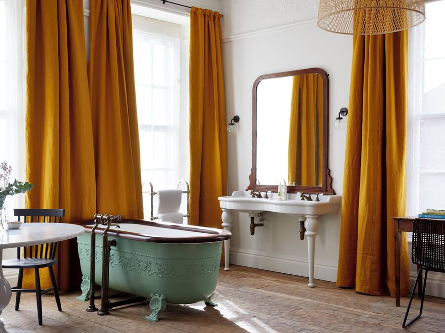 A bathroom with a vintage clawfoot bathtub, a white sink with a mirror, and yellow curtains.