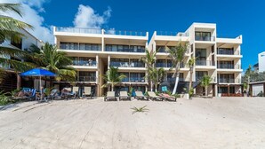 A beachfront hotel with multiple balconies, a sandy beach, and palm trees. - Beautiful beach level condo, perfect for a family, pool access, WiFi, AC! (Akumal)