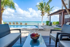 A poolside area with lounge chairs, a table with a bowl of fruit, and a view of the ocean. - Beautiful beach level condo, perfect for a family, pool access, WiFi, AC! (Akumal)
