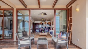 A spacious living area with wicker furniture, a ceiling fan, and a view of the kitchen and dining area. - Beautiful beach level condo, perfect for a family, pool access, WiFi, AC! (Akumal)
