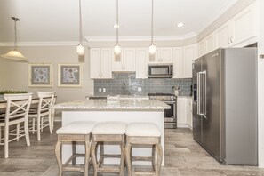 A modern kitchen with white cabinets, a stainless steel refrigerator, a granite countertop, and pendant lighting.