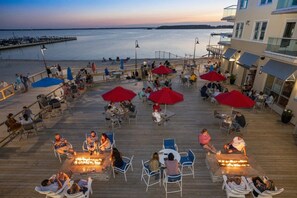 Una terraza de madera con mobiliario exterior y fogones, con vista a un cuerpo de agua y un muelle.