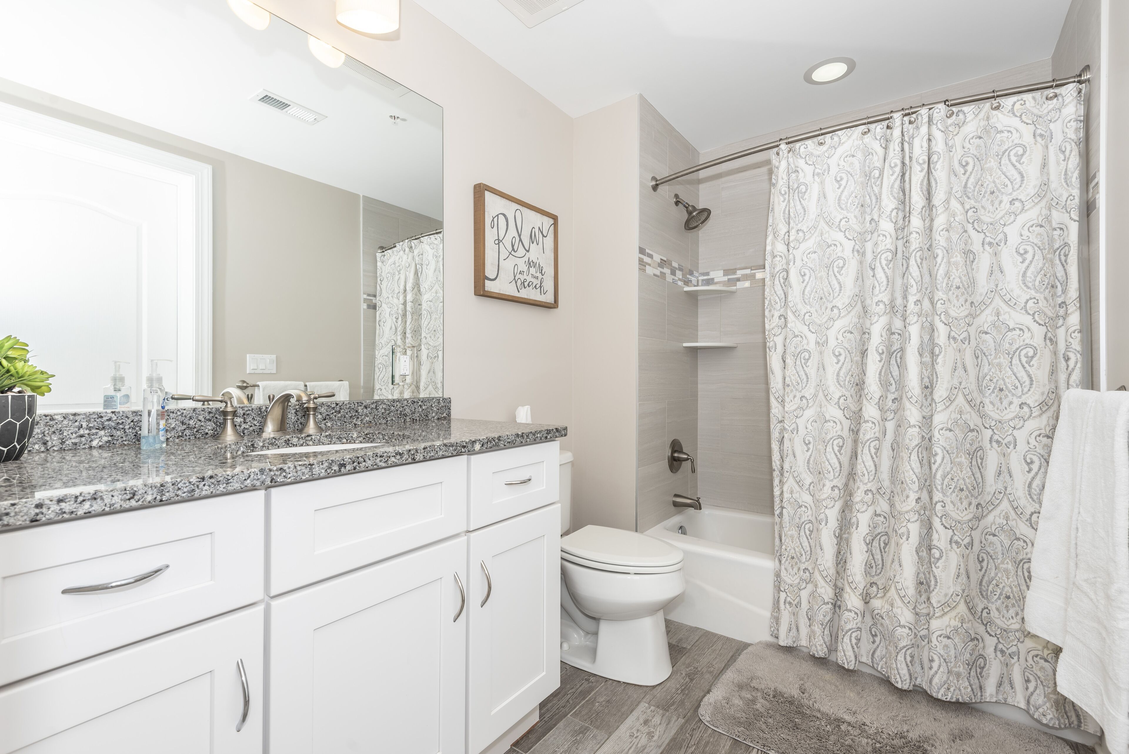 A modern bathroom with a granite countertop, white cabinetry, a toilet, a bathtub, and a shower curtain.