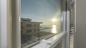 Ett fönster med utsikt över en byggnad och en vattenyta, en vit handduk på fönsterbrädan och en vit gardin som delvis är uppdragen.