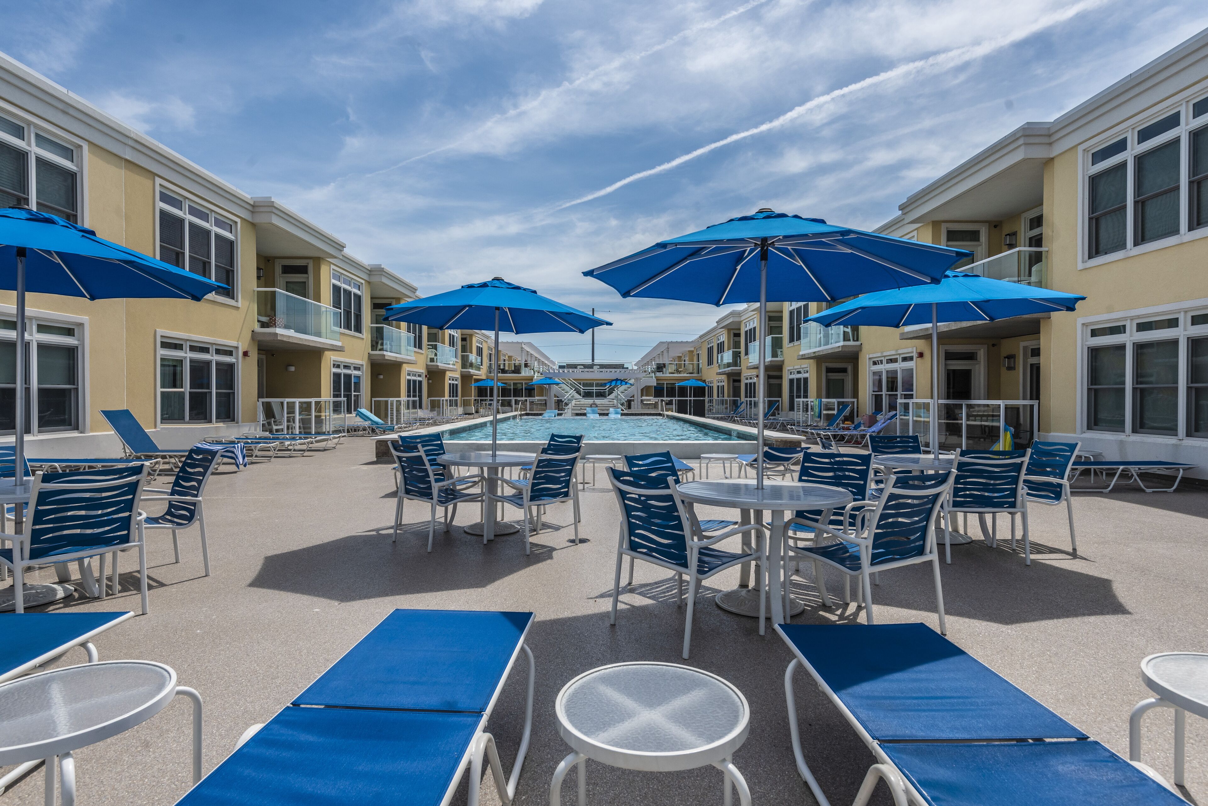 Un espace aménagé au bord de la piscine, avec des parasols bleus, des chaises longues et des tables.
