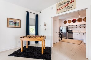 Une pièce avec une table de baby-foot, un panneau indiquant le « Kentucky Bourbon Trail », une photo encadrée d’une course de chevaux, et une cuisine équipée d’un four à micro-ondes et d’un lave-vaisselle.