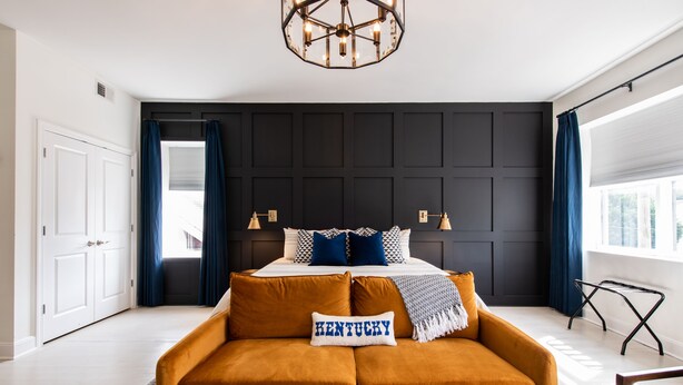 Ein modernes Schlafzimmer mit einem großen Bett, einem senfgelben Sofa und einem Zierkissen mit der Aufschrift "KENTUCKY".