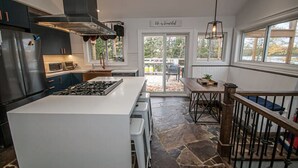 Une cuisine moderne dotée d’un îlot central, d’appareils électroménagers en acier inoxydable et d’un revêtement de sol en pierre.